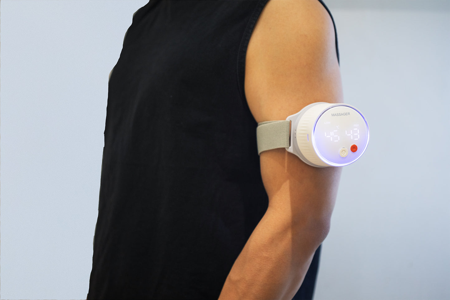 Side view of a man in a black sleeveless shirt wearing a smart moxibustion device on his muscular upper arm, standing against a bright white wall.