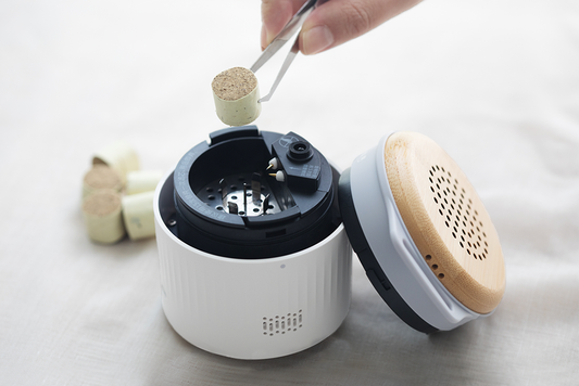 Close-up of a smart moxibustion device with its lid open, a hand using tweezers to place a moxibustion stick inside, demonstrating the product’s precise and user-friendly operation.